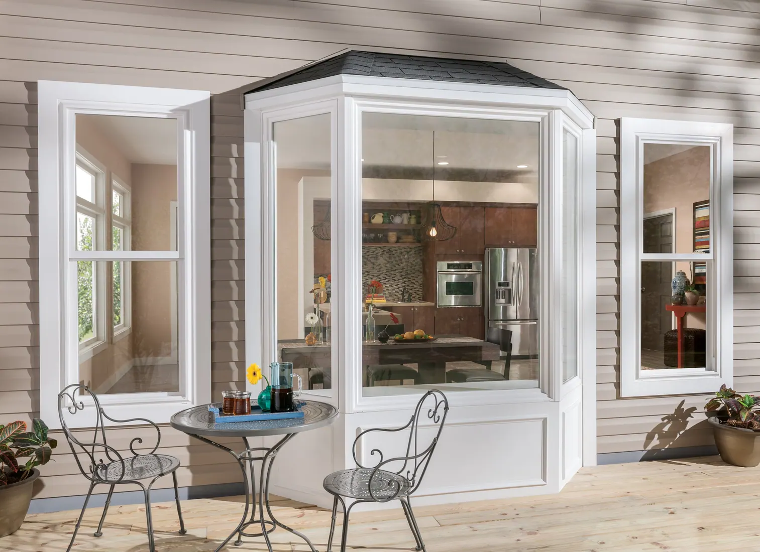 Exterior view of white Milgard Tuscany Series bay windows beside a patio